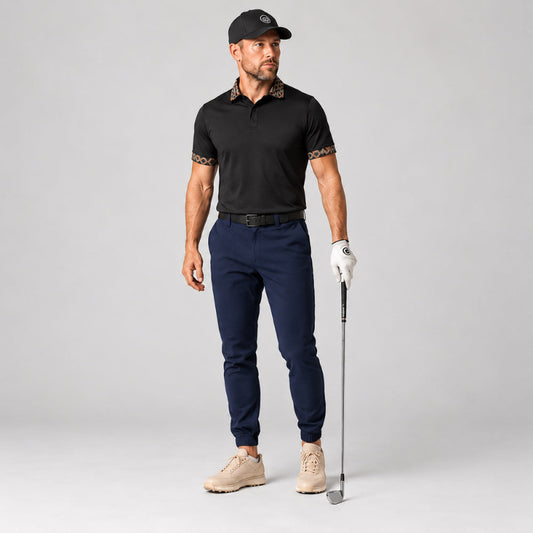 A male model stands on a light gray studio background wearing a black short-sleeve polo shirt with patterned trim on the collar and sleeve cuffs, navy golf pants, a white golf glove, beige golf shoes, and a black cap. He is holding a golf club.