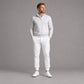 A man modeling a light gray quarter-zip pullover sweater and white jogger pants with white golf shoes, standing against a solid gray studio background.