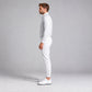 A man in a light grey long-sleeve quarter-zip pullover and white joggers stands in profile against a light gray studio background, wearing white athletic shoes.