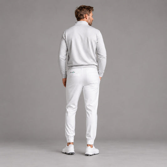 A man is shown from behind wearing a light gray long-sleeve quarter-zip pullover and matching white jogger pants with white golf shoes, set against a solid gray studio background.